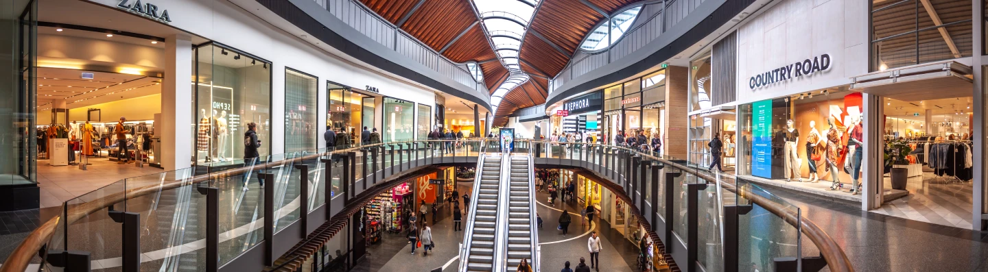 Multi-level Australian shopping centre with escalators and retail stores illustrating real-world store traffic analytics.