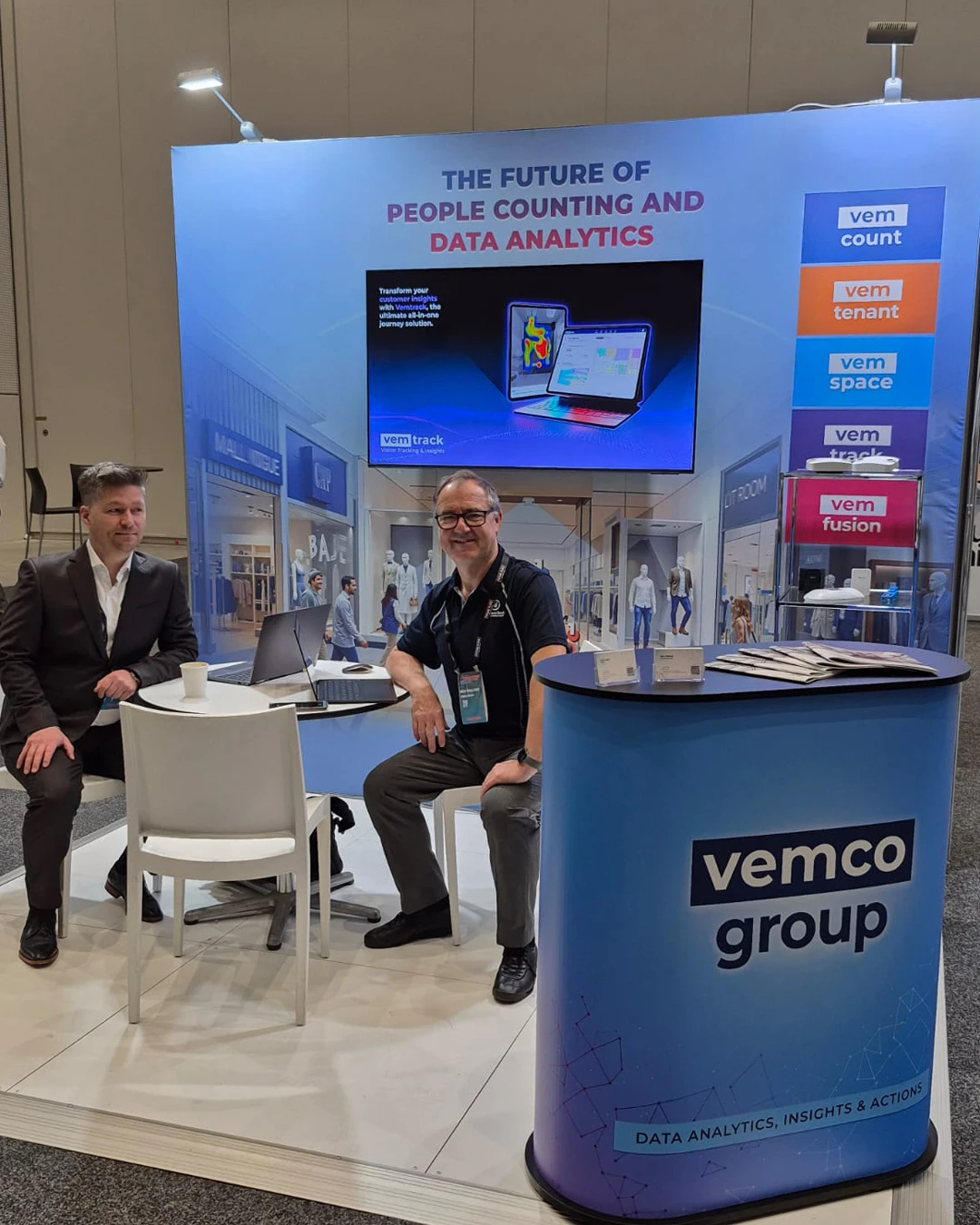 The Cohera Tech exhibition stand at the Malls of the Future conference, showing the full booth setup with a display screen