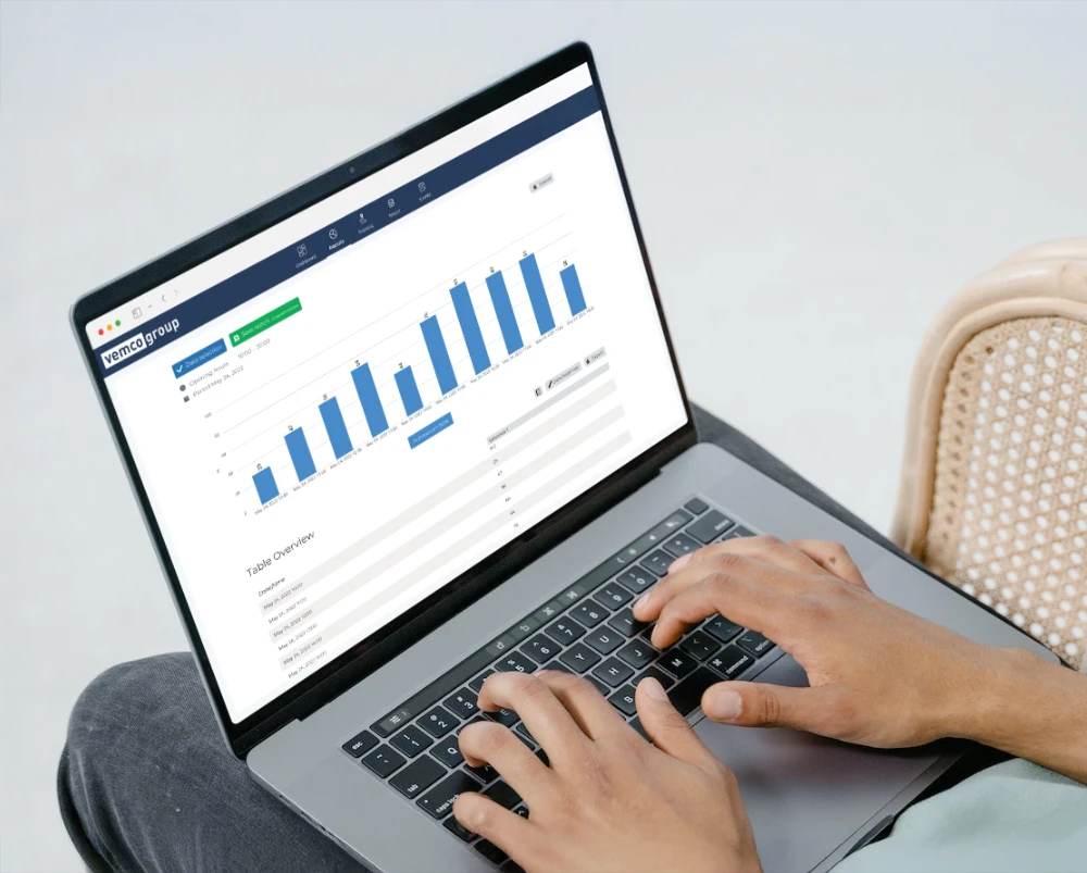 Laptop screen displaying the VemCount people counting analytics dashboard with bar charts and data table